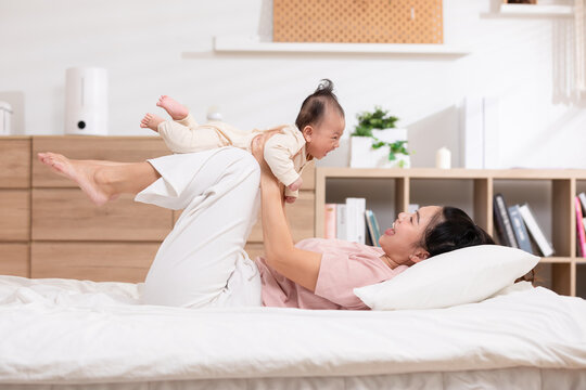 New asian mom playing to adorable newborn baby on bed smiling and happiness at home.Mom talking with infant baby and laughing throwing up her son in the air together.Relax time.Baby and Mother day
