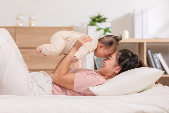 New asian mom playing to adorable newborn baby on bed smiling and happiness at home.Mom talking with infant baby and laughing throwing up her son in the air together.Relax time.Baby and Mother day