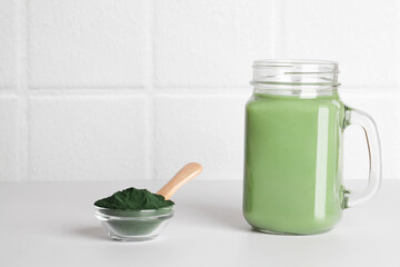 fresh green smoothie in glass bottle and spirulina powder with spoon on ceramic tile background. self care and healthy lifestyle. copy space