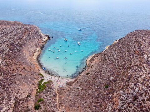 Aerial drone, Cala Pulcino in Lampedusa, 
tranquil cove with rugged landscape, clear waters, known as "caletta barche volanti" or "flying boats cove"