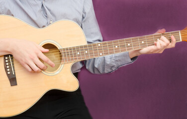 Fototapeta na wymiar Young man playing guitar on dark purple background with copy space