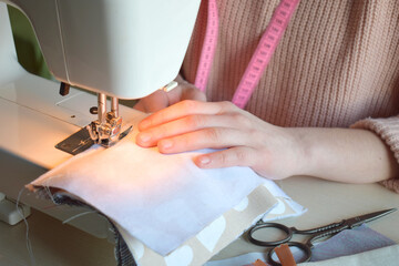 Sewing process. Female hands are sewing fabric on a sewing machine at the workplace. Hands of a seamstress hold textiles for the production of clothing or accessories