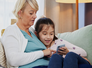 Can you download this game for me, gran. Shot of a little girl using a cellphone while sitting at home with her grandmother.