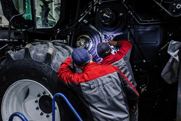 Service workers repairing agricultural harvester in workshop