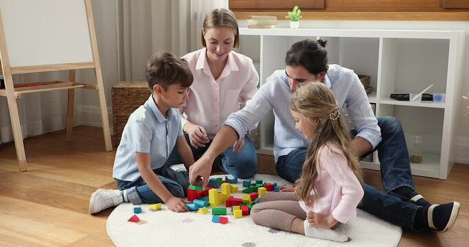 Couple and children enjoy wooden bricks game at home. Parents with little son and daughter sit on floor in nursery play colored blocks, talk, having pleasant family leisure. Kids development concept