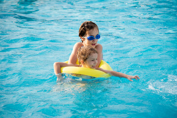 Two young smiling girls in a swimsuit bathes play in a pool with blue clear water in blue swimming glasses. Summer. Rest. Vacation.