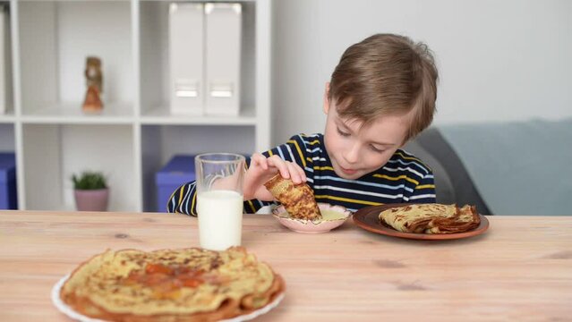 Caucasian child boy eats pancakes with appetite, dipping them in condensed milk. Baby food and diet concept