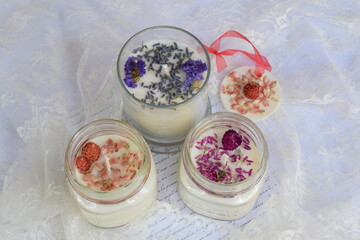 Hand-poured scented soy candles with scented sachet on table with lace. 