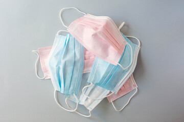 Medical masks of blue and pink color lie on top of each other on a gray background. The topic of protecting health from coronavirus and cancellation of medical masks.