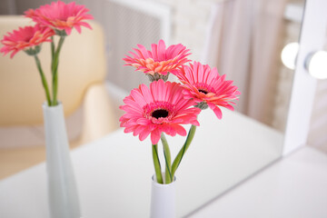 Bouquet of beautiful pink gerbera flowers in vase on table near mirror