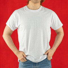 White t-shirt for mock-up print design. A young man wears a short-sleeved t-shirt, jeans, studio shot on a red background. Guy in white clothes for advertising