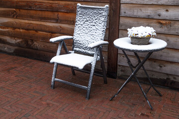 Snowy garden chair garden table against a wooden fence.