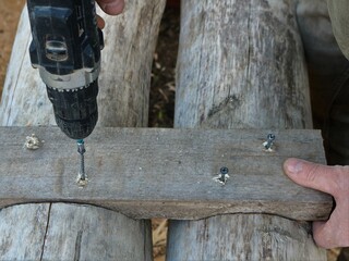 screwing fasteners into the structure of a wooden structure with a screwdriver, mechanically fastening parts from an aged gray textured wood with a screw, close-up of work with a screwdriver