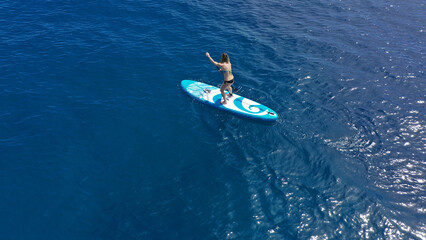 Aerial drone photo of fit unidentified woman paddling on a SUP board or Stand Up Paddle board in deep blue sea