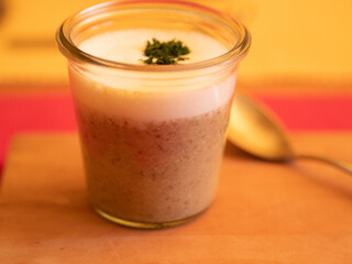 Champignon cappucino with milk froth and parsley, served in a glass on a wooden board