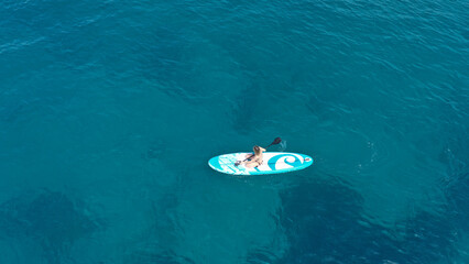 Aerial drone photo of fit unidentified woman paddling on a SUP board or Stand Up Paddle board in deep blue sea