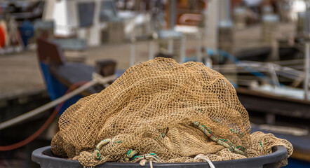 Ein Fischernetz in einer Tonne mit Hafen im Hintergrund. 