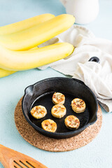 Fried banana slices in a frying pan and fruits nearby on the table. Homemade sweet snacks. Vertical view