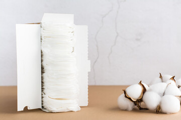 A box with clean disposable sanitary pads and a branch of cotton on the table. Women's health and comfort concept