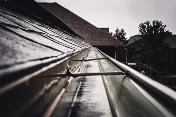 Selective focus on a section of residential guttering with hanger conveying water during a storm....