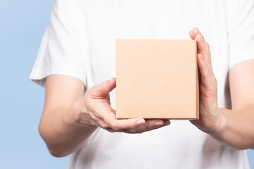 Female hands holding brown rectangular cardboard box on light blue background. Mockup parcel box. Packaging, shopping, delivery concept