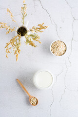 Oat milk in a glass, oatmeal in a bowl and ears in a jug on a light table. Alternative plant food. Vertical view.