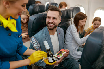 Stewardess giving champagne to man in passenger airplane