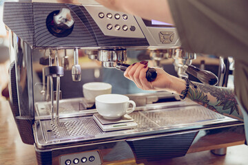 Young woman barista using coffee machine in coffeehouse