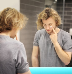 young man looking in the mirror,combing his hair,looking at problems on face.