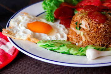 Fried rice with chinese sausage served in a white plate with fried egg, tomato and lettuce.