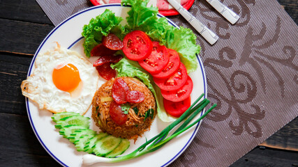 Fried rice with chinese sausage served in a white plate with fried egg, tomato and lettuce.