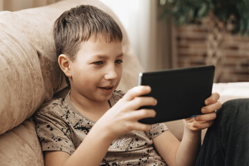 Teenage boy sitting on couch using tablet and playing video games on internet online at cozy home.