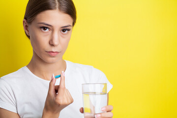 Woman holding pill and glass of water taking dietary supplements.