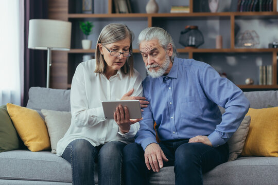 Senior couple family retired man and woman watching online consultation on video call. Two elderly patients listen a doctor or lawyer who gives advice using a tablet smartphone phone remotely at home