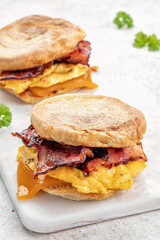English muffin, scrumbled egg, ham, and cheese breakfast sandwich on a cutting board