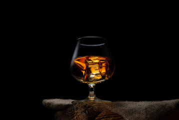 a glass of whisky with ice cubes on black background