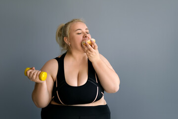 A fat obese woman greedily eats a donut while holding a dumbbell in her other hand. The lady could...