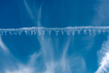 Die von Wind zerzausten Cirruswolken vor blauem Himmelshintergrund mit Kondensstreifen...