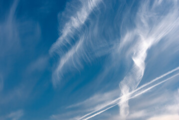Die von Wind zerzausten Cirruswolken vor blauem Himmelshintergrund mit Kondensstreifen...