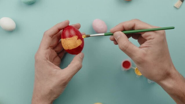 Hand of a man is painting colored Easter eggs