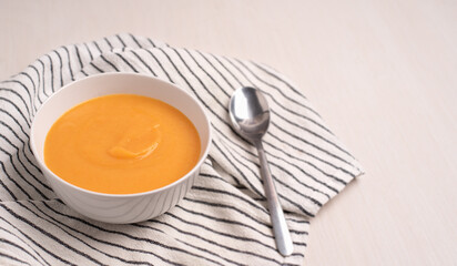 A bowl of pumpkin soup with a spoon on a light background. Healthy food, vegan food. 