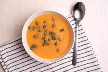 A bowl of pumpkin soup with a spoon on a light background. Healthy food, vegan food. Top view, flat lay. 