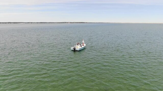 Wide aerial rotating around small fishing boat in Cape Cod Bay in emerald green water in summer