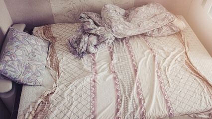 Unmade bed with wrinkled bedsheet and blanket in teenage bedroom at morning time view from above