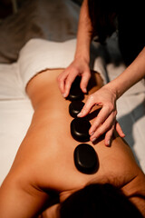 The masseuse massages the girl's back with hot stones. Hot stone massage in the spa.