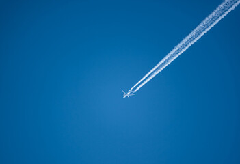 looking up at a KLM Boeing 787 Dreamliner twin engine jet airliner in deep blue sky with vapour contrails diagonally across the frame