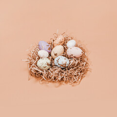 Naklejka na ściany i meble A simple spring and Easter concept. A few Easter colorful eggs in a bright nest. The eggs are of different sizes and decorated with a golden texture. Minimal composition. Light pastel background.