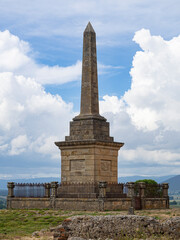 Monolito memorial en medio de la naturaleza, sobre un cielo azul nuboso en Soria, verano de 2021.