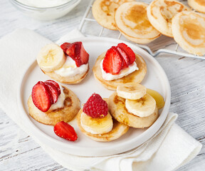 Trendy food pancake cereal with fruits, honey, yogurt. Heap of mini cereal pancakes in bowl on light background.