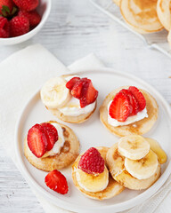 Mini pancake cereal with banana, raspberry, strawberry, honey, yogurt for breakfast. Mini pancake cereal is new trend. Mini pancakes cereal served for breakfast, snack. Selective focus, copy space.